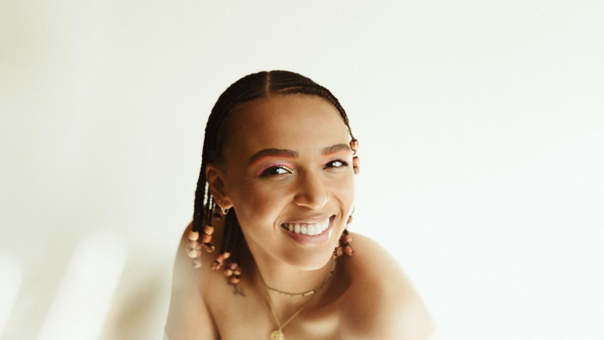 Smiling person with braids and colorful eye makeup against white background