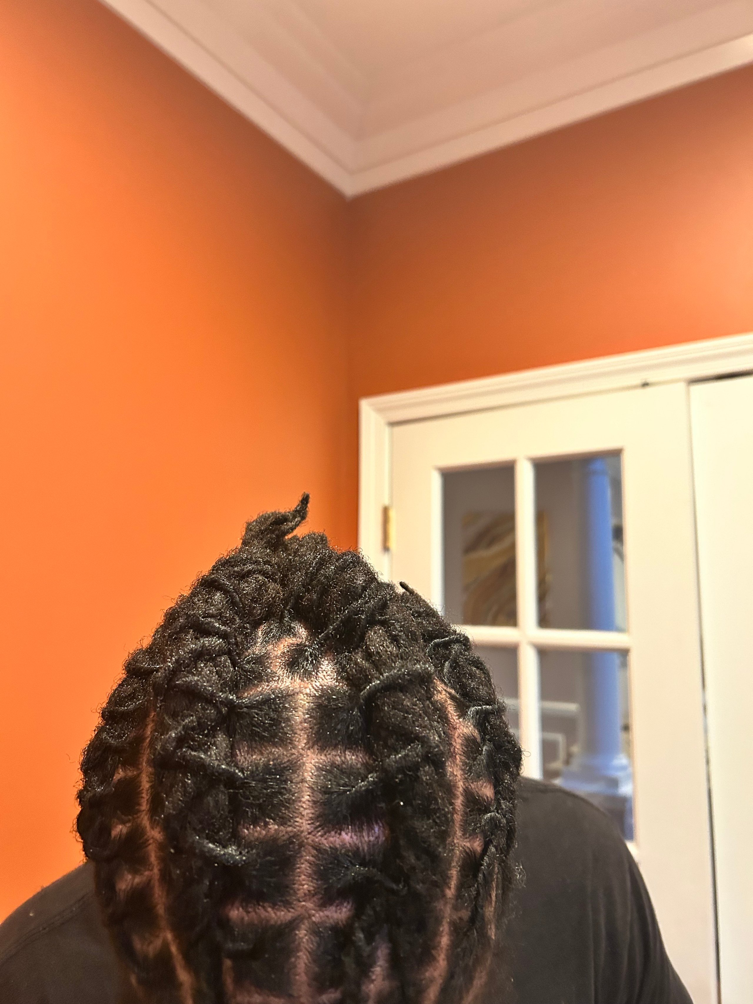 Detailed view of braided hair against an orange wall with a window