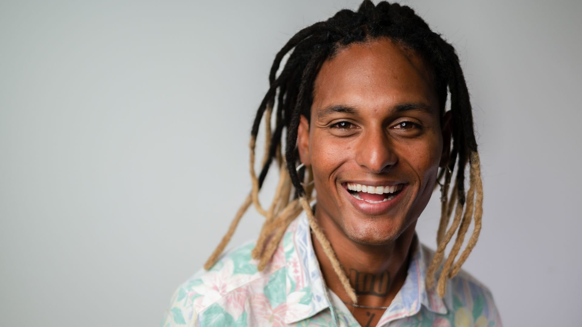 Person with dreadlocks wearing pastel shirt, laughing brightly