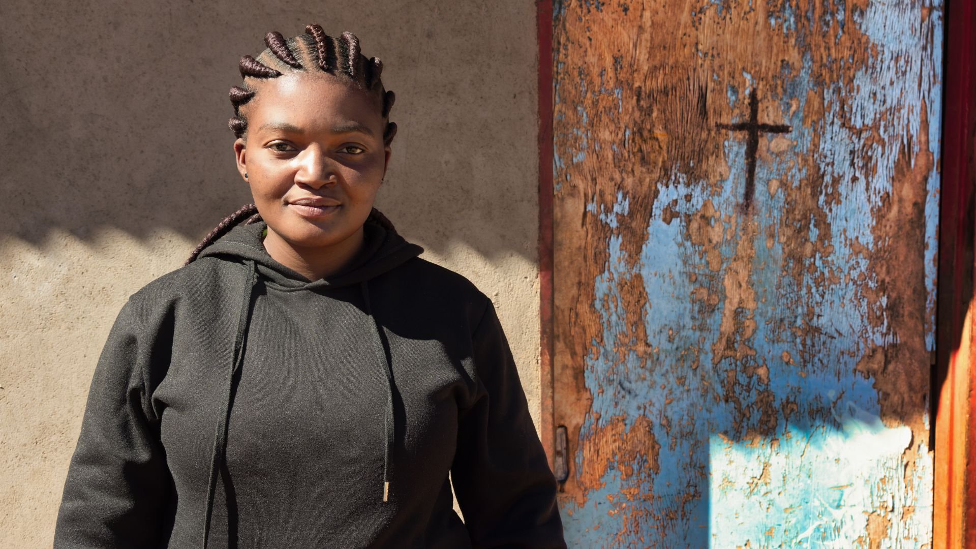 Person in black hoodie standing near weathered blue and brown wall
